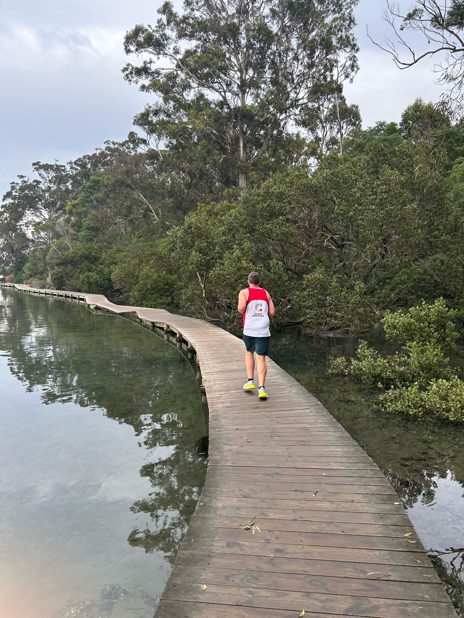 Person running on a wooden boardwalk next to water with bushland background